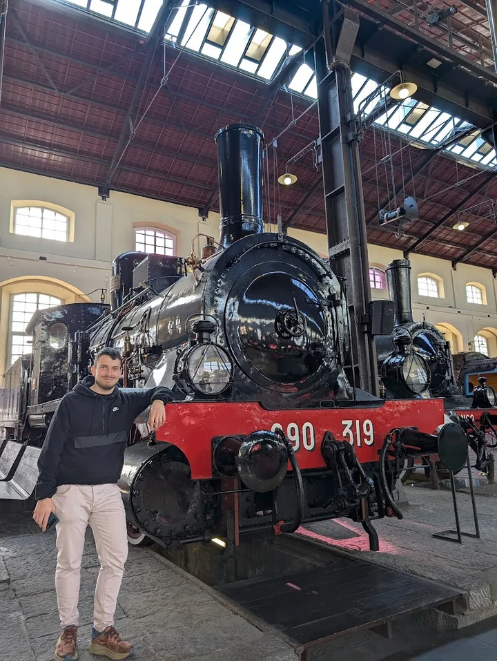 Davide standing beside a preserved steam locomotive in a railway museum