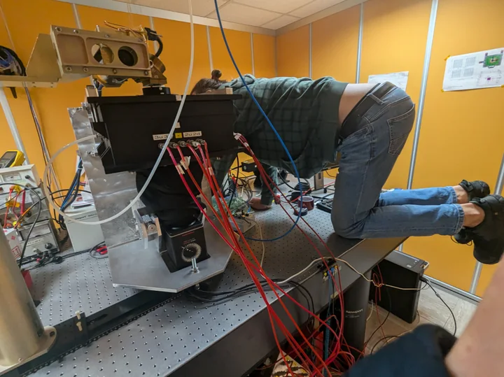 A researcher working on the polarimetry apparatus, with readout cables and gas lines on an optical bench